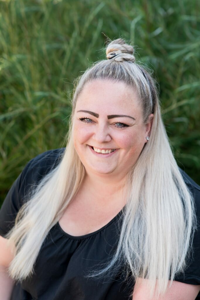 Eine junge Frau mit einem strahlenden Lächeln. Blond gefärbten Haaren, die zu einem Knoten auf dem Kopf gebunden sind